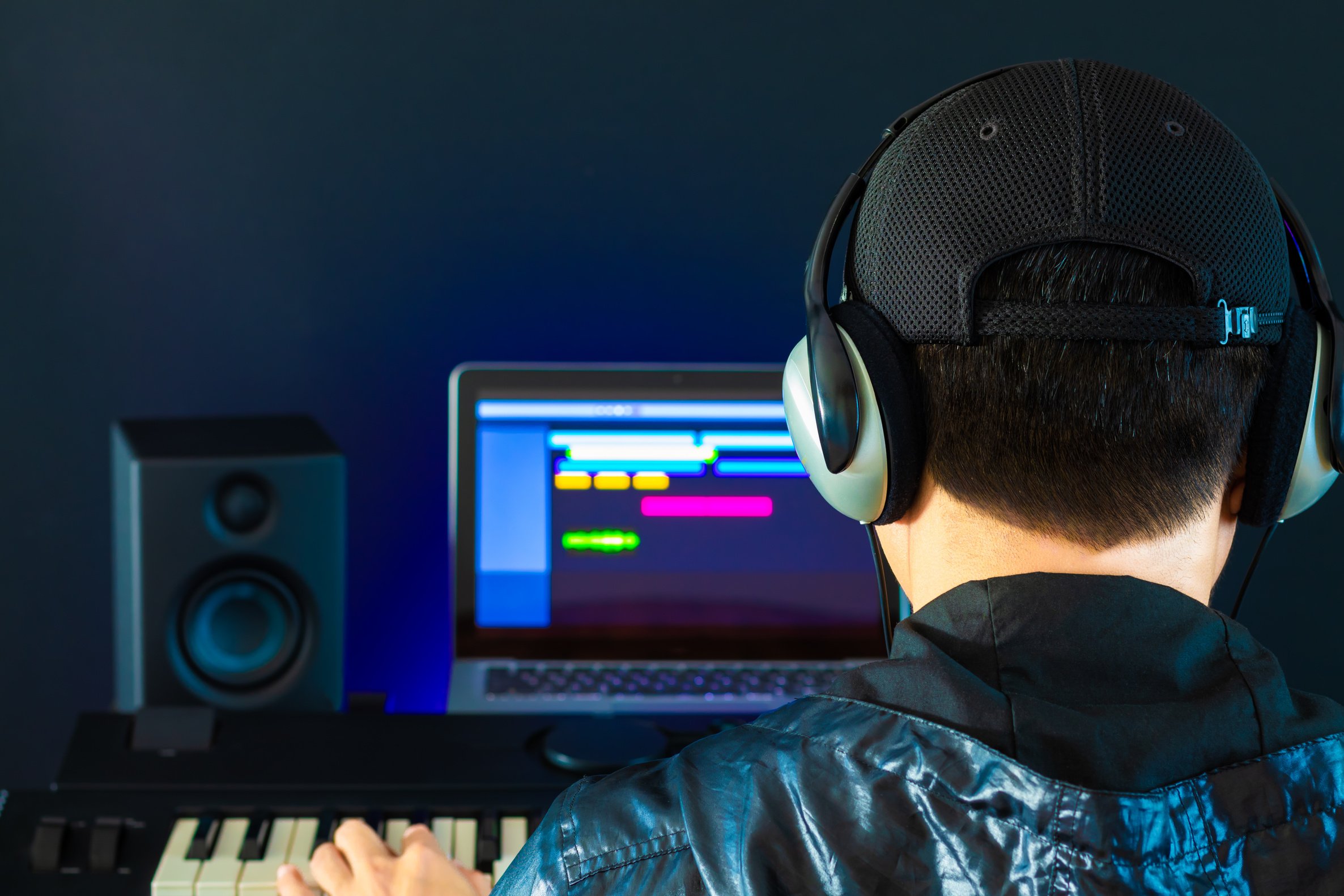 back of asian professional male music producer, sound engineer arranging a song on midi keyboard, laptop computer. music production concept